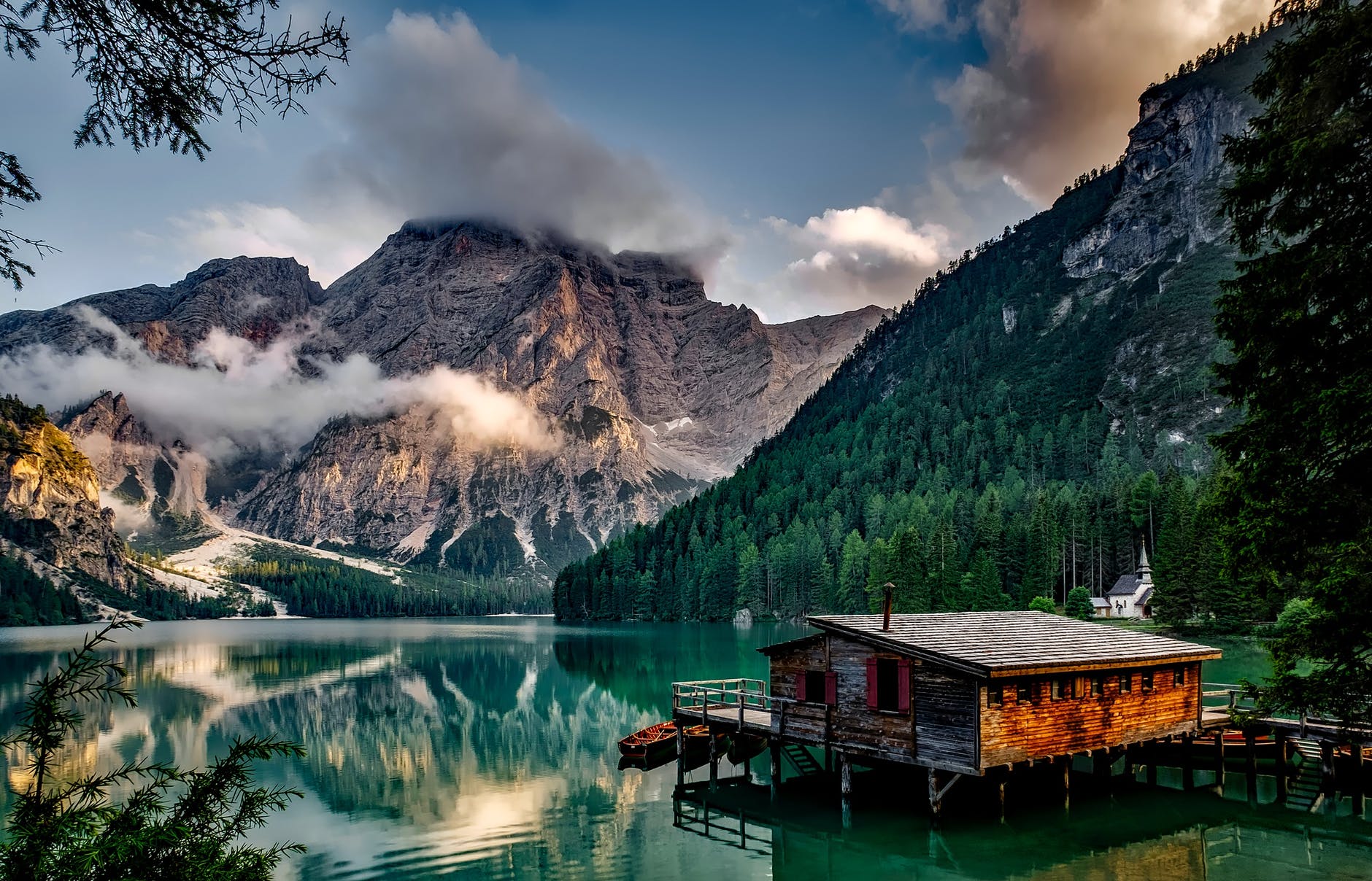 mirror lake reflecting wooden house in middle of lake overlooking mountain ranges