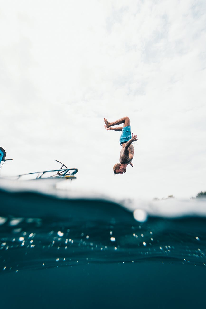 man wearing blue shorts about to dive on body of water