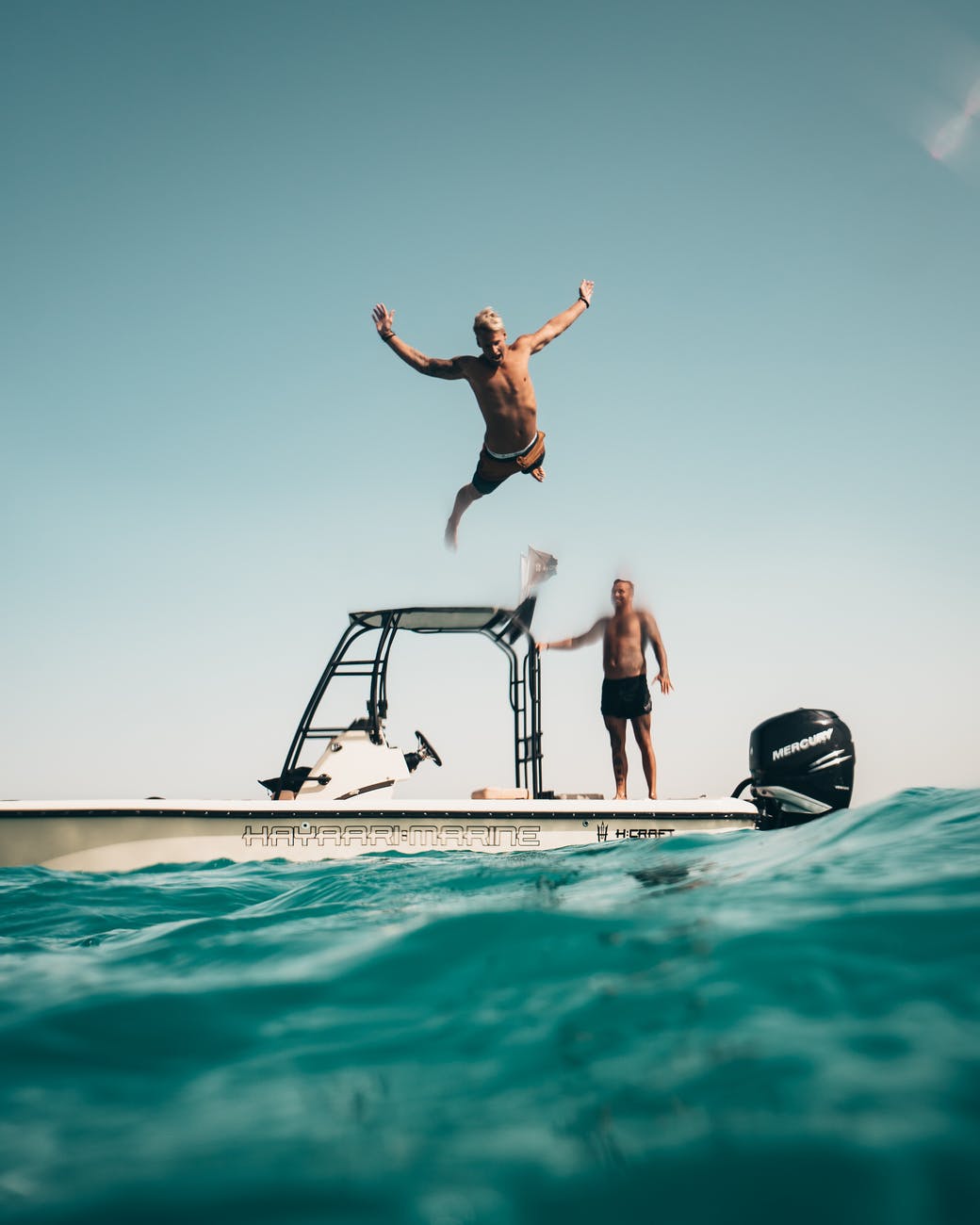 photo of man jumping from boat to the sea