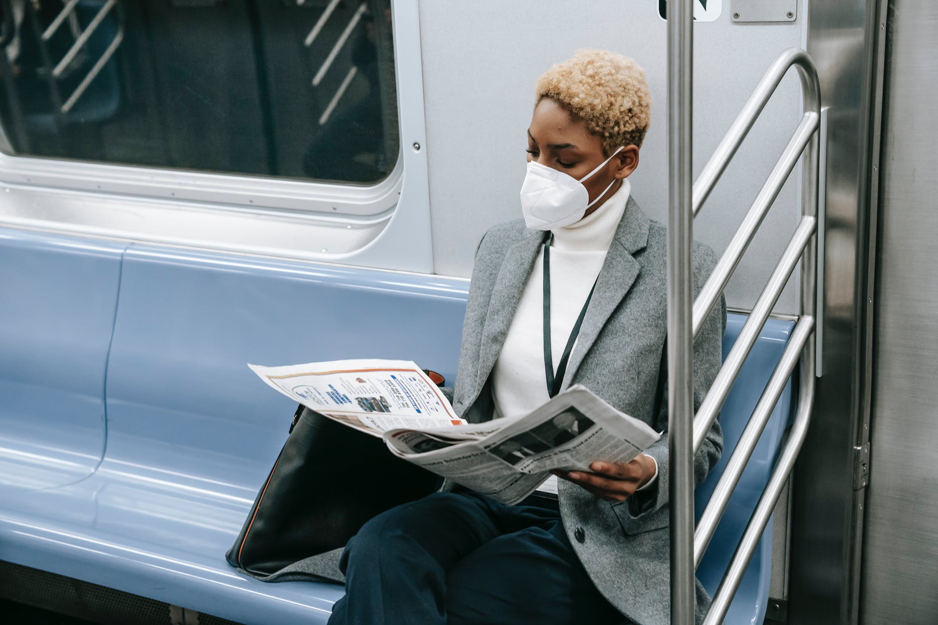 serious black lady in medical mask reading newspaper in train