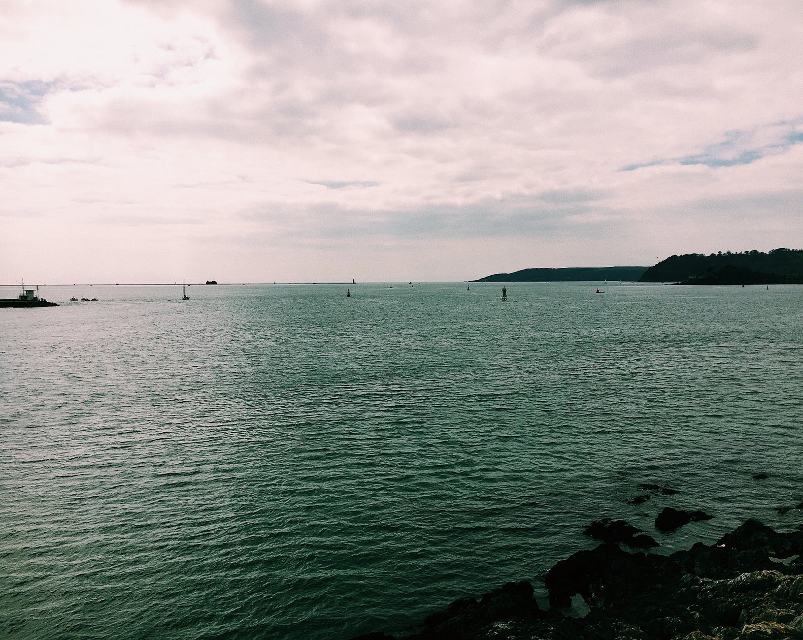 rocky shore near ocean with boat under cloudy sky