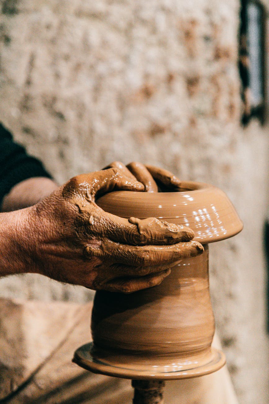 man creating pot with clay in yard