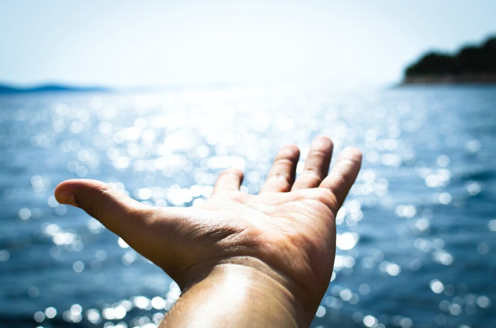 person hand reaching body of water