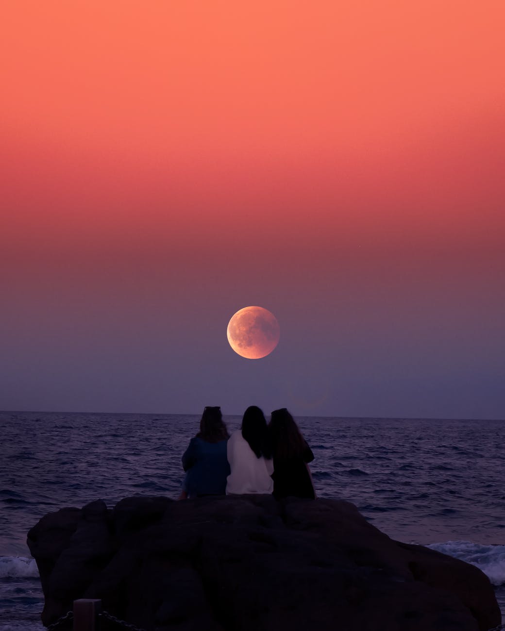 three women sitting on rock infront of ocean