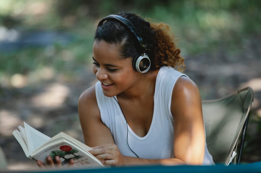 smiling ethnic woman with headphones reading book