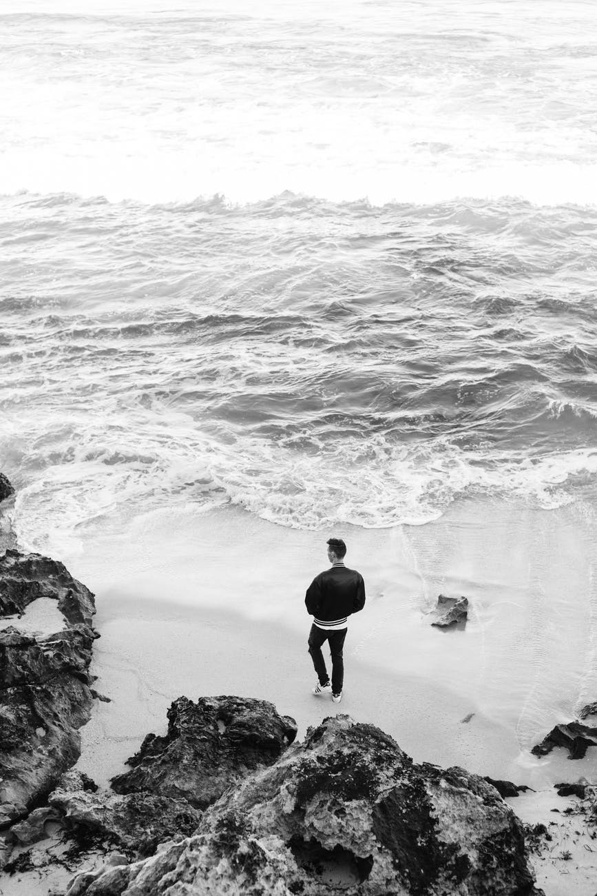 unrecognizable man standing on waving seashore