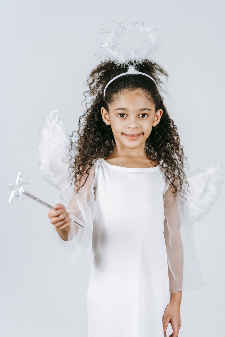 smiling ethnic little girl with rod in angel costume looking at camera