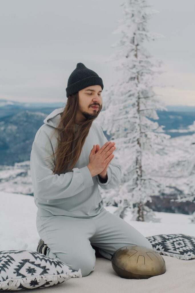 man with namaste hands sitting on snow with hapi drum