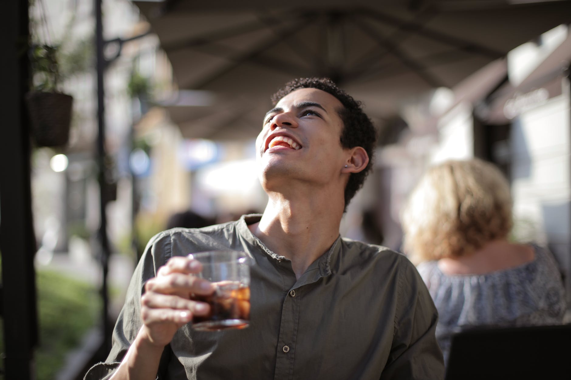 happy ethnic man having drink with ice cubes in street cafe in sunny hot day