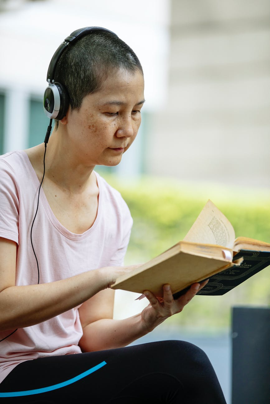 asian lady in headphones reading book in street