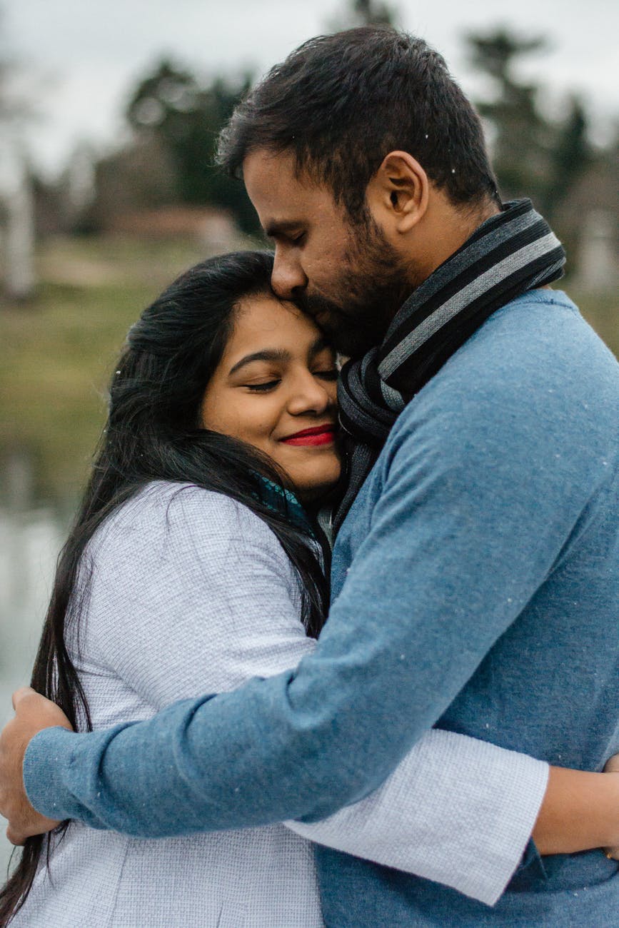 man in blue kissing woman on forehead