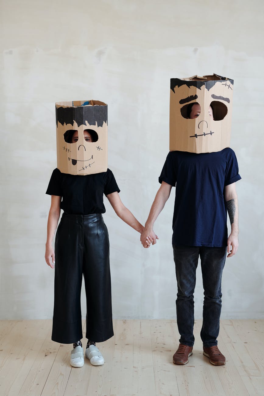 a couple wearing diy cardboard box mask while holding each other s hands