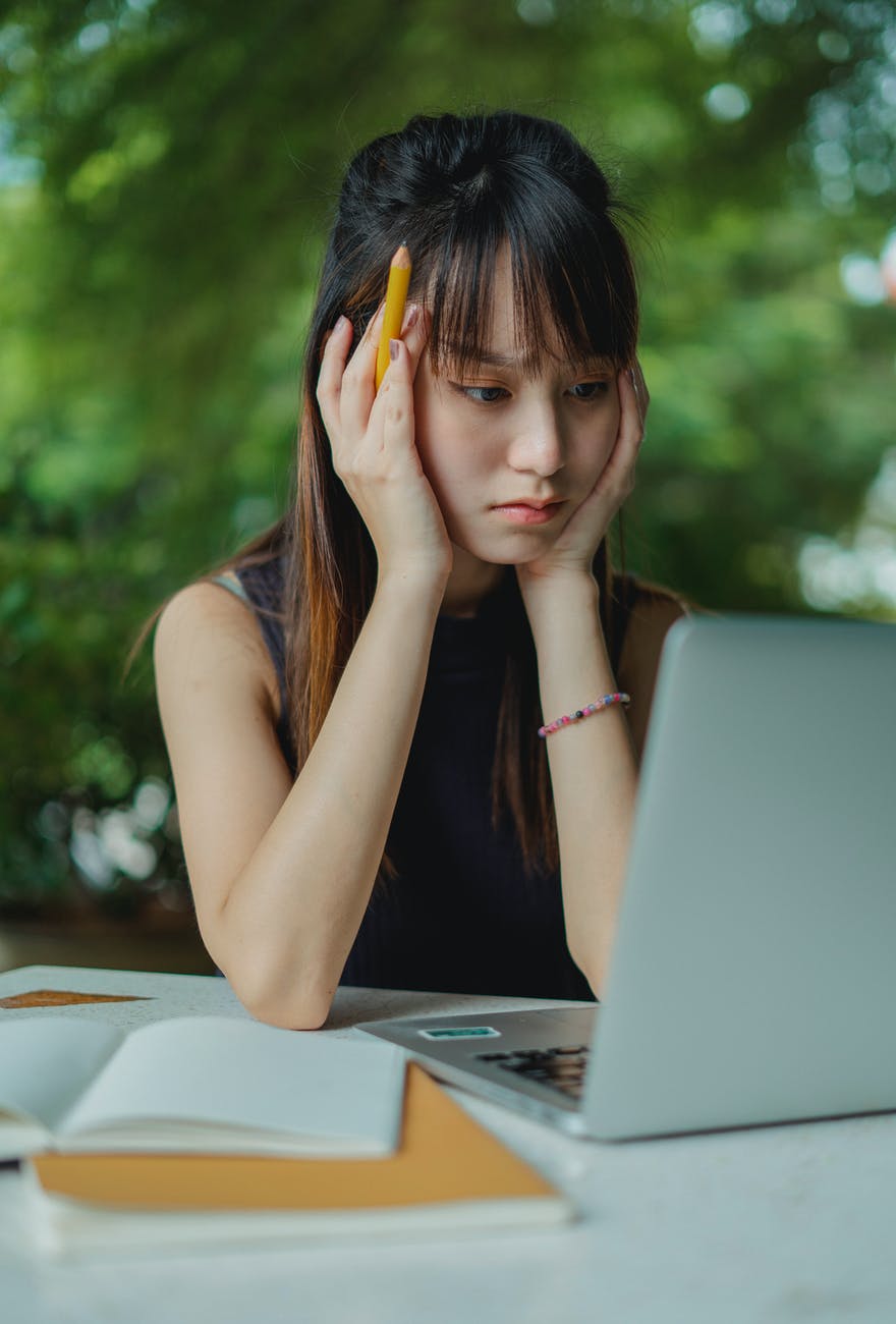 thoughtful young asian woman working on laptop in street cafe